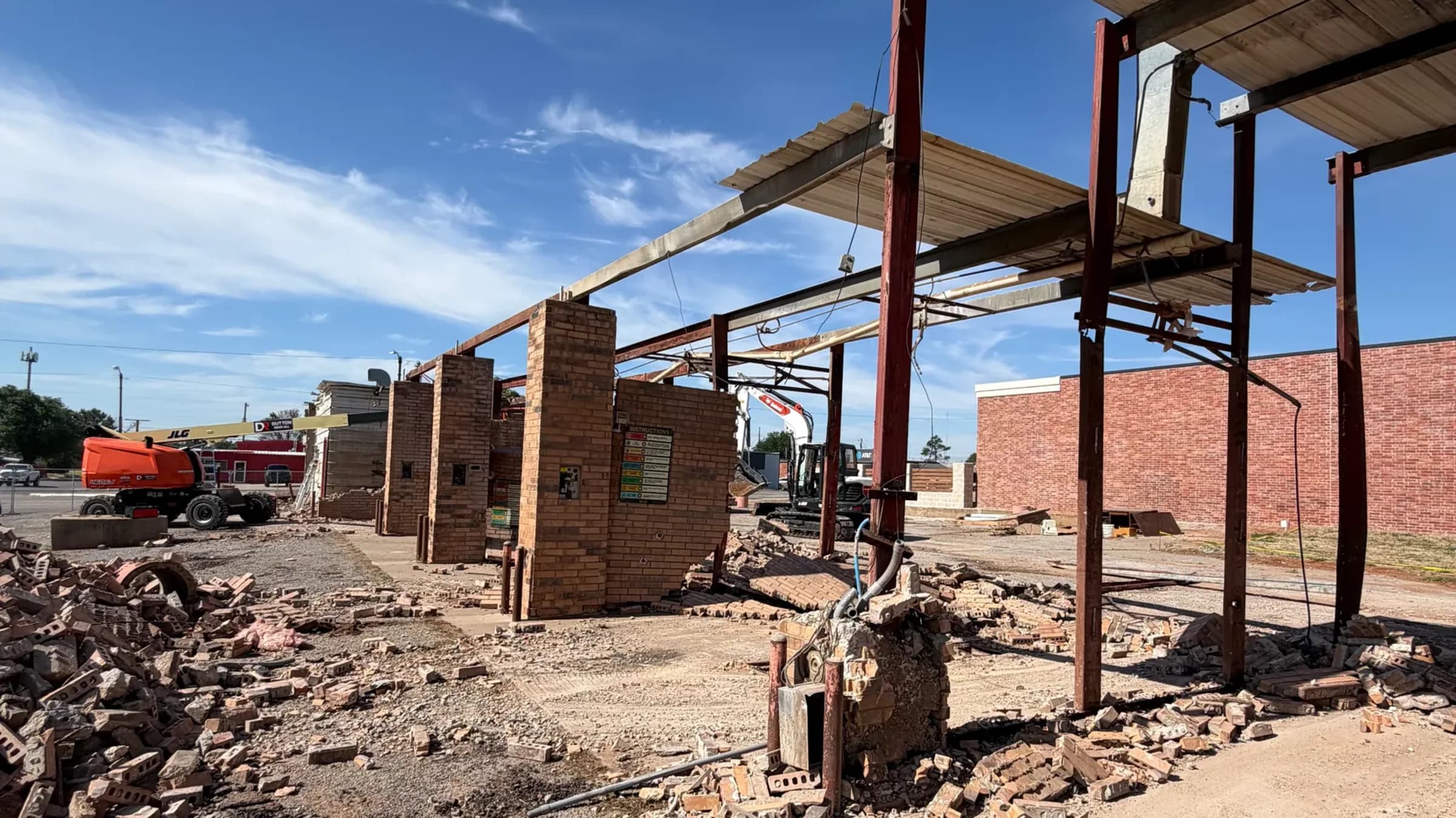 Piles of broken brick where the car wash walls stood, with only the steel canopy frame and one brick column still up.